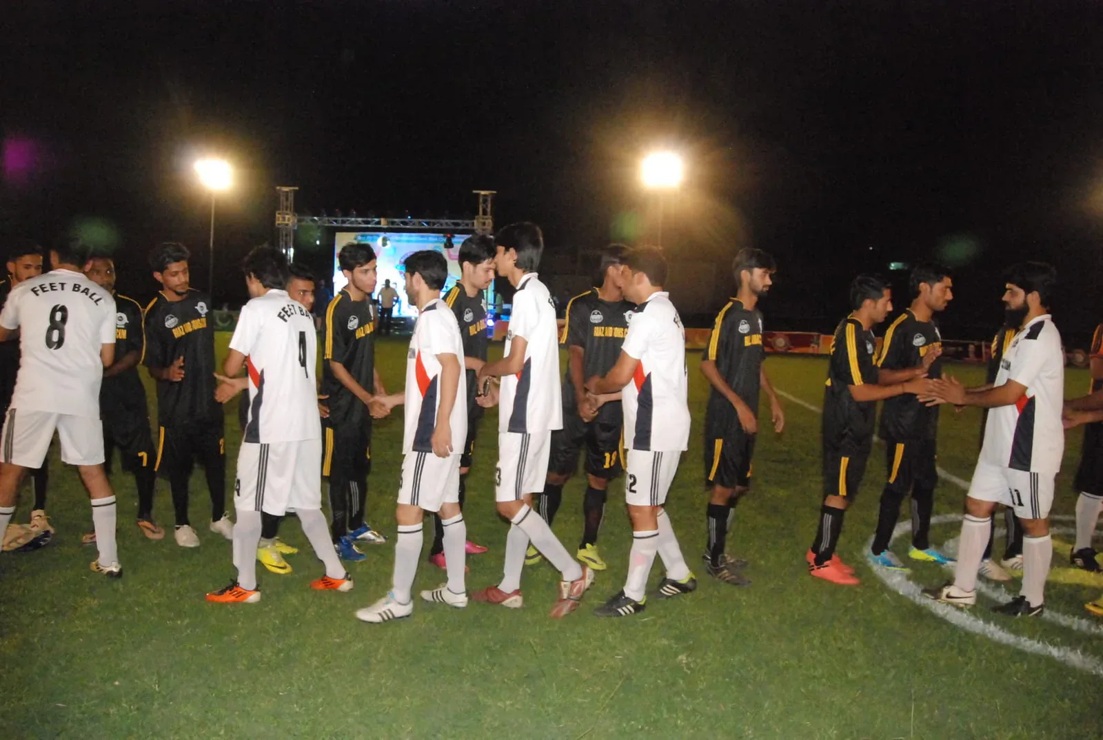 Players shaking hands in the pre-match line at a floodlit Feetball fixture